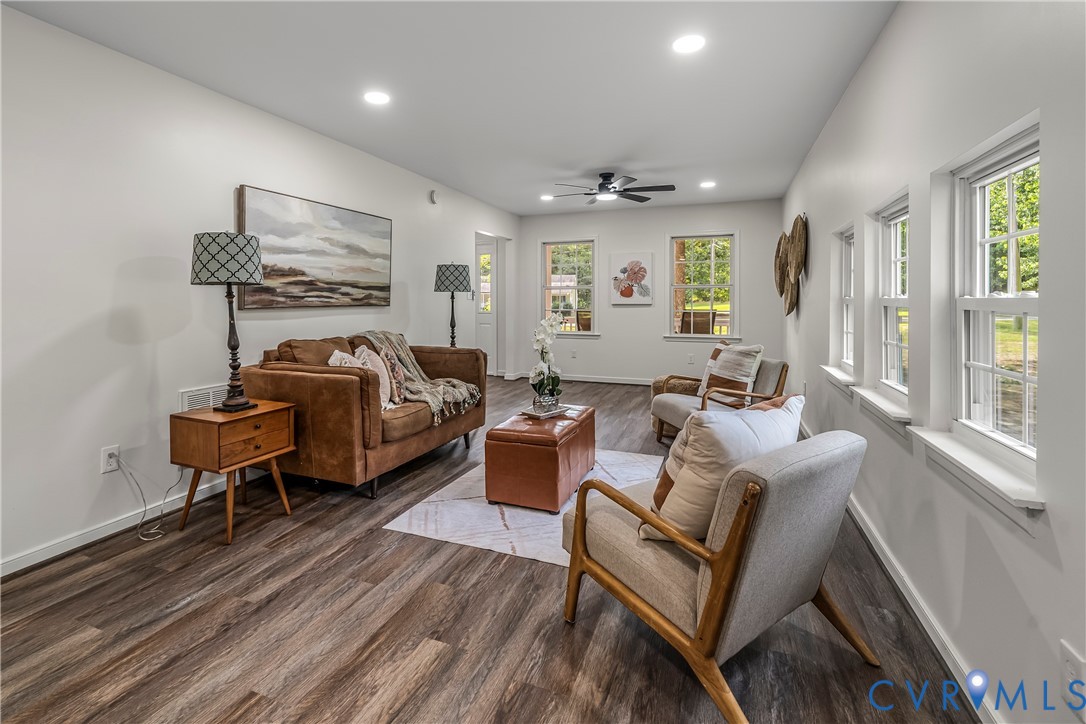 Staged living room with brown sofa, gray chairs, leather ottoman, and large windows.