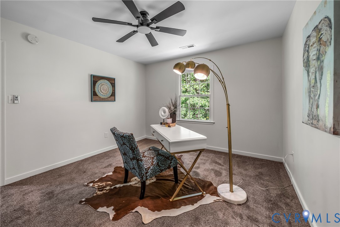 Furnished home office with a white desk, patterned chair on a cowhide rug, and brass floor lamp.