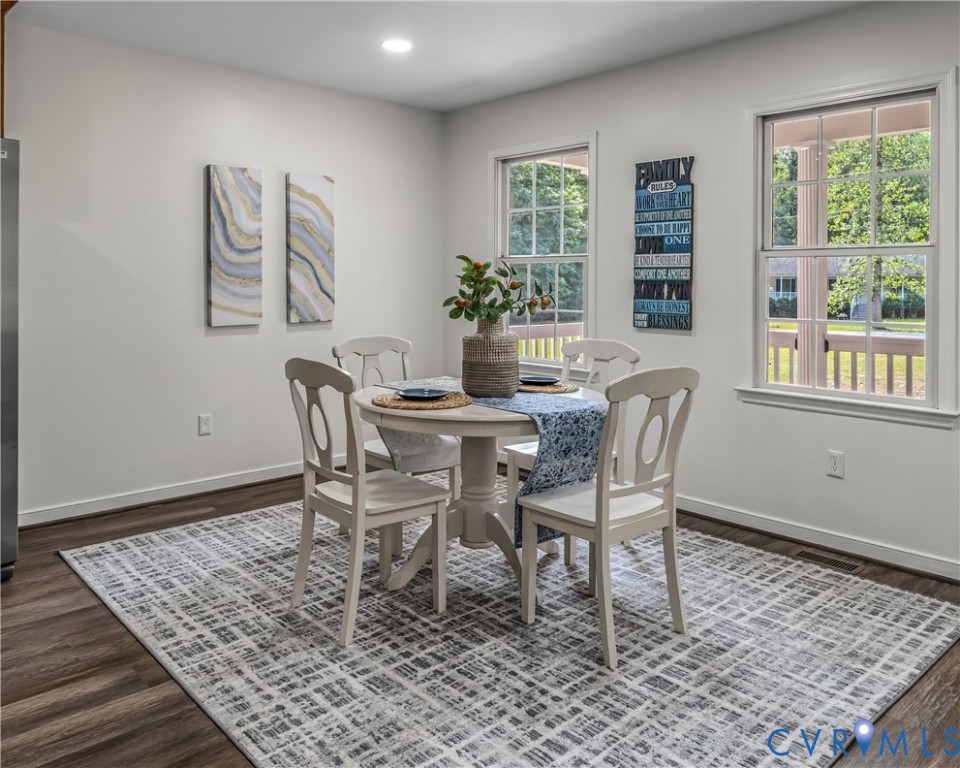 Dining room with a round white table, four chairs, patterned rug, and two bright windows.