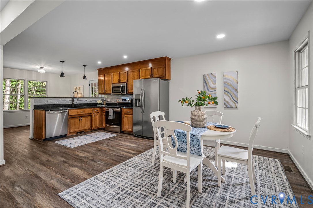 Kitchen and dining area with warm wood cabinets, stainless steel appliances, and a white table by large windows.