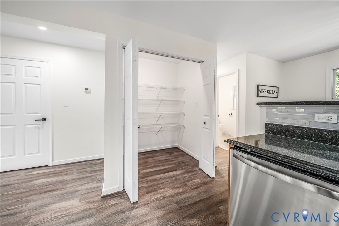 Kitchen pantry with open wire shelving beside dark granite counters and a stainless steel dishwasher.