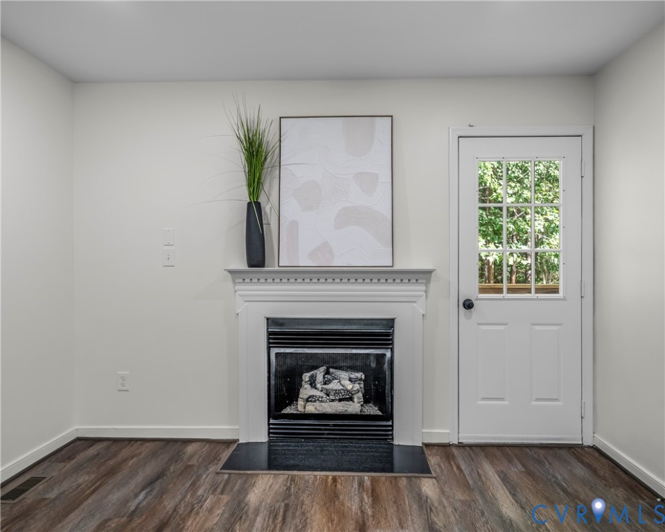 Unfurnished room with a white fireplace and windowed exterior door overlooking trees.