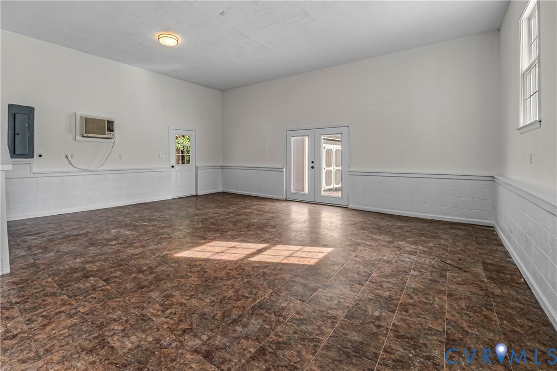 Empty room with brown tile floors, white wainscoting, and glass exterior doors.