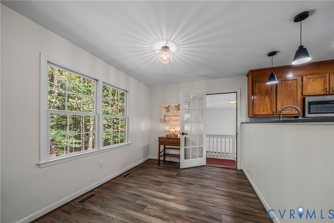 Kitchen and dining area with wood cabinets, wood-look floors, and large windows overlooking trees.