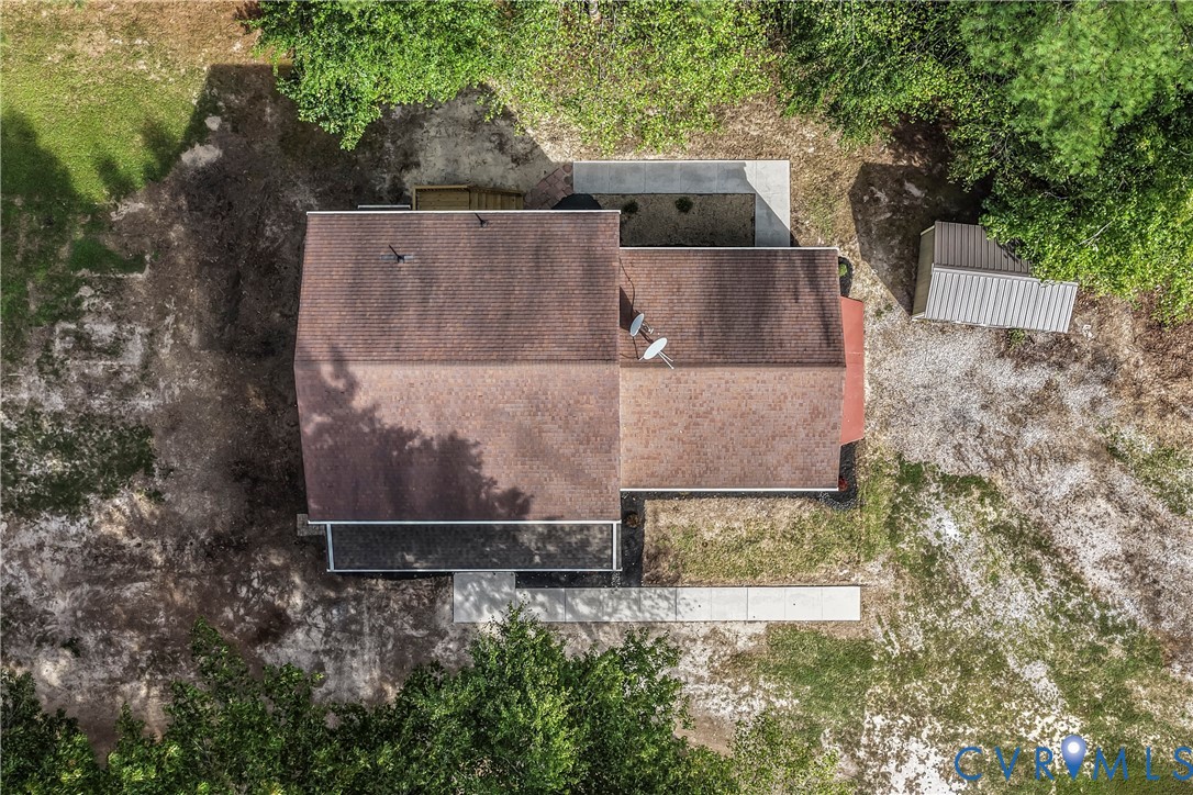 Aerial view of a home with a brown shingle roof, concrete patio, and surrounding trees.