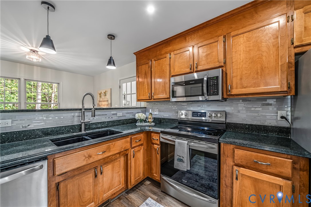 Kitchen with warm wood cabinets, dark counters, stainless steel appliances, and a double-basin sink.