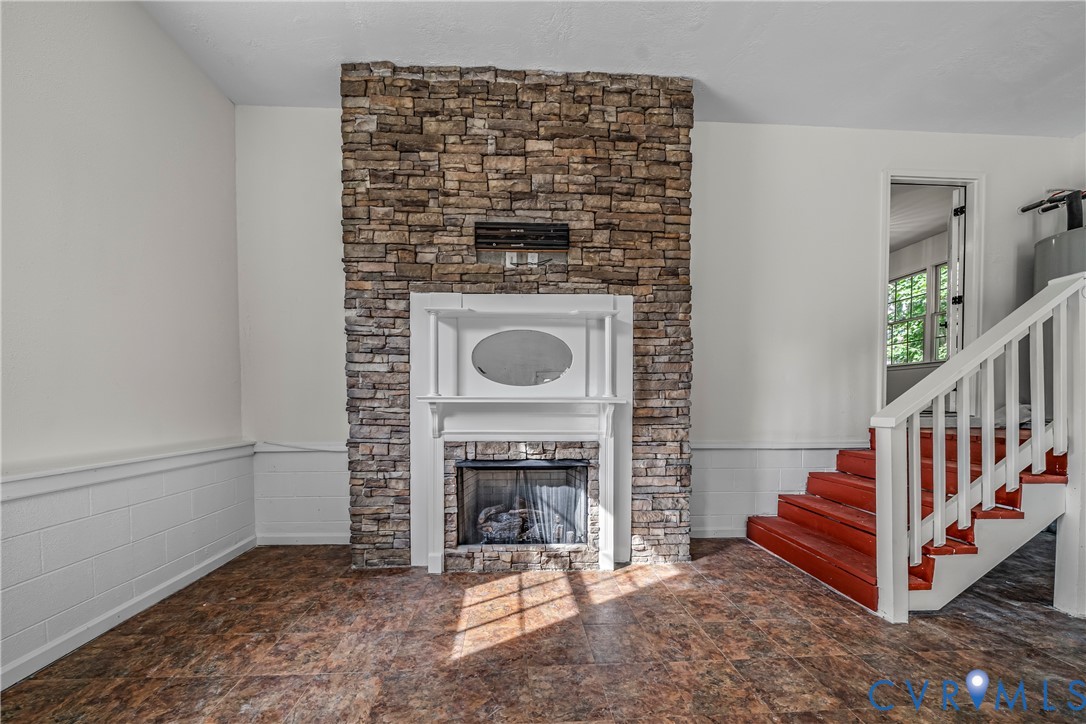 Room with a tall stone fireplace and red staircase.