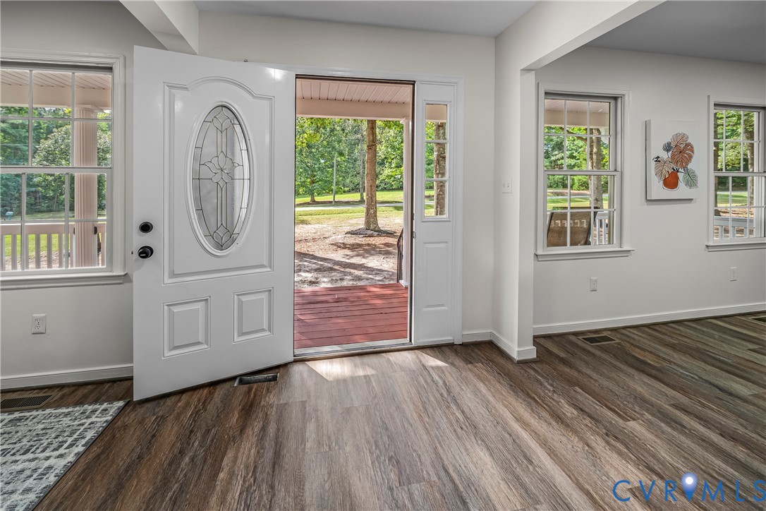 Entry with an open oval-glass front door, wood-look floors, and windows overlooking the covered porch.