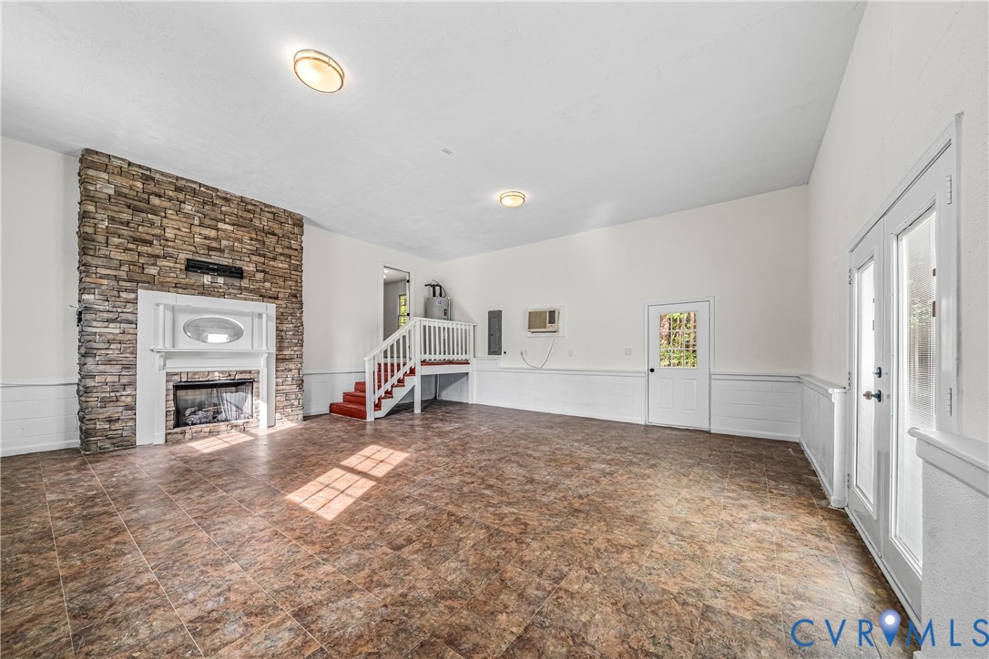 Vacant living room with a stone fireplace, brown tile floors, and a raised stair landing.