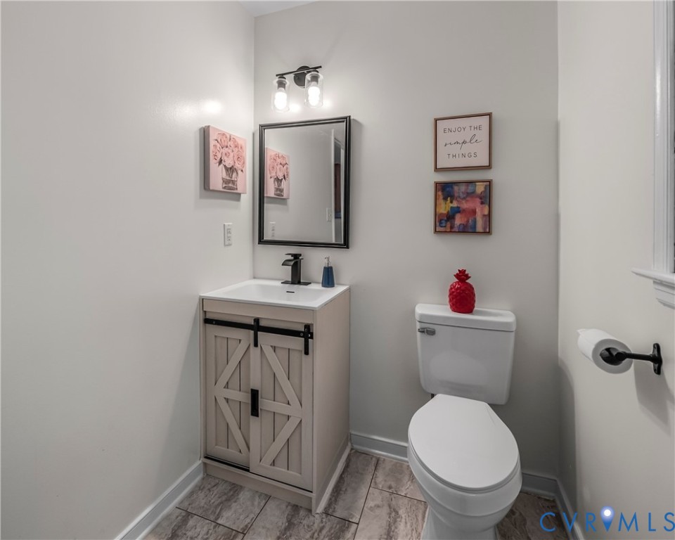 Bathroom with a light wood barn-door vanity, black faucet, framed mirror, and white toilet.