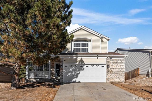 Two-story beige home with stone accents and a white double garage, partly obscured by an evergreen tree.