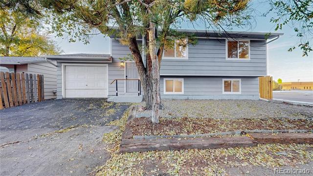 Gray split-level house with an attached garage, broad driveway, and a mature tree in the front yard.