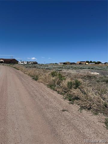 Open scrubland beside a dirt road, with scattered homes in the distance.