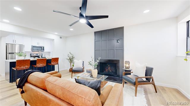 Living room with caramel leather sofa, dark paneled fireplace, and open kitchen with orange bar stools.