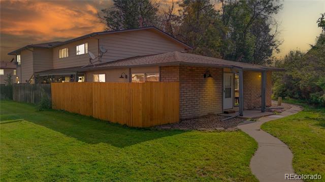 Single-story brick-and-siding home behind a wooden privacy fence, with a curved walkway and lawn at dusk.