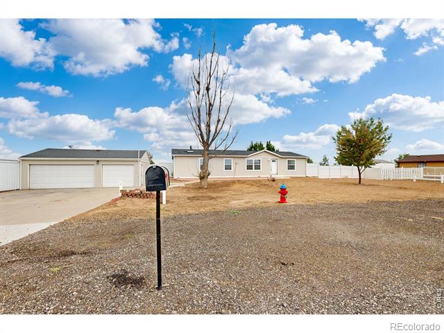 Single-story house with a two-car garage, broad gravel yard, and leafless tree.