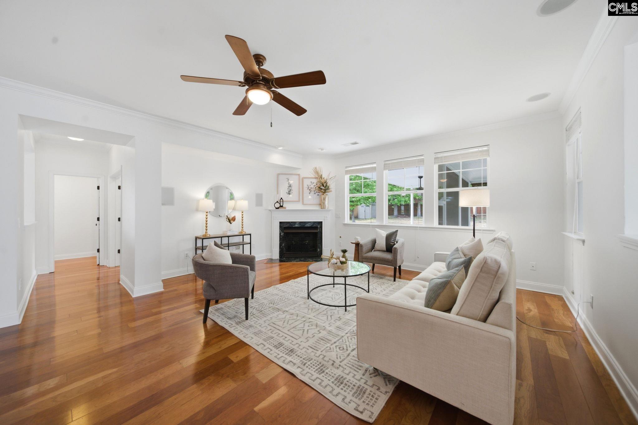Living room with hardwood floors, a white fireplace, and large windows.
