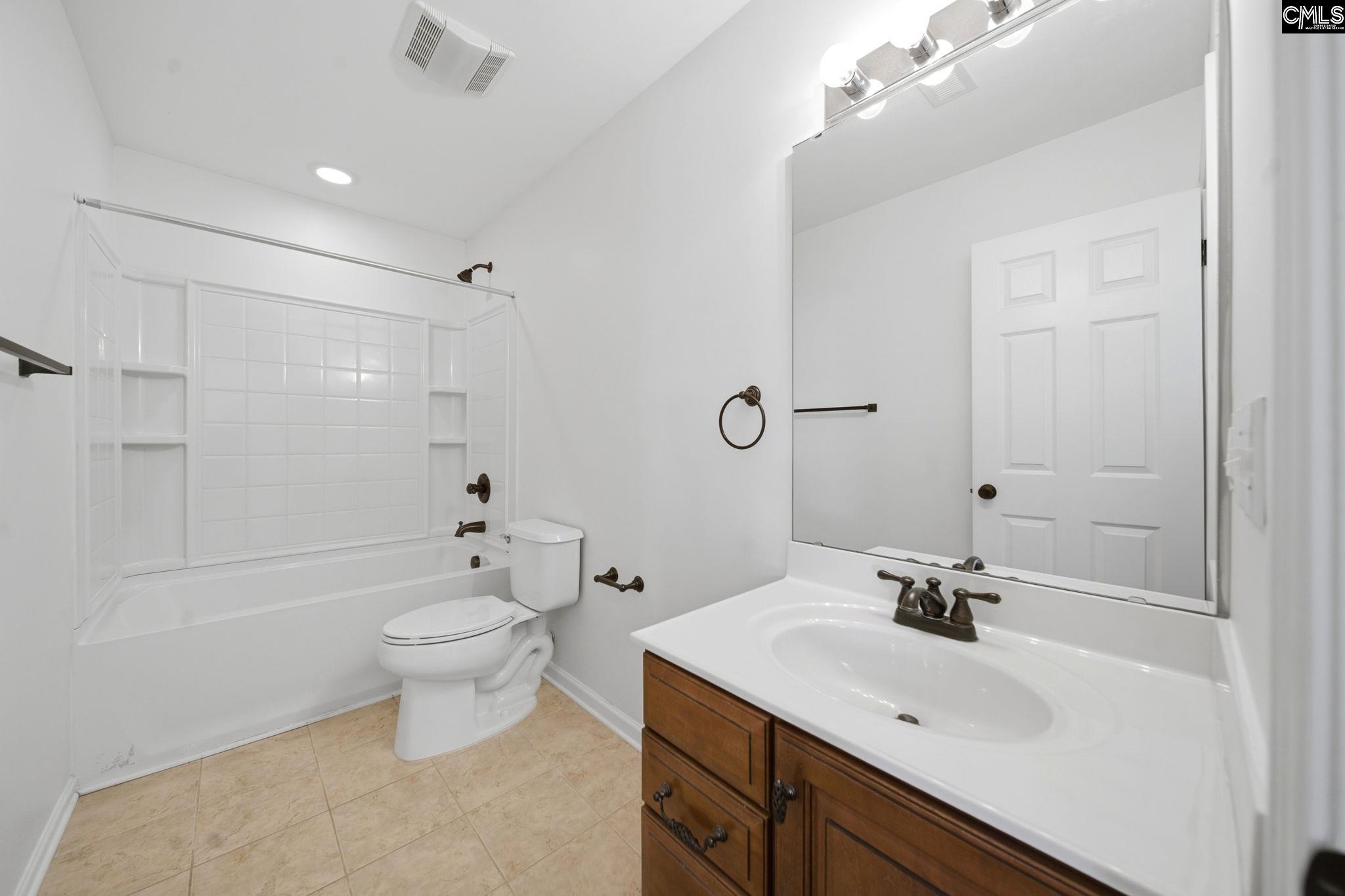 Bathroom with a white tub and shower, toilet, and wood vanity with a large mirror.