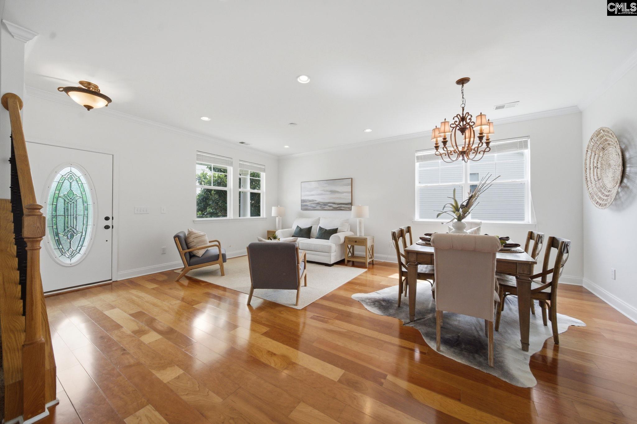 Open-plan living and dining room with hardwood floors, a white sofa, and an oval glass front door.