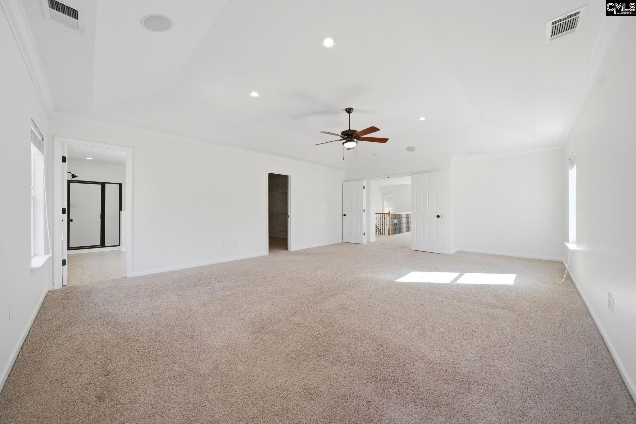 Vacant carpeted bedroom with a ceiling fan, high ceiling, and open doors to adjoining rooms.