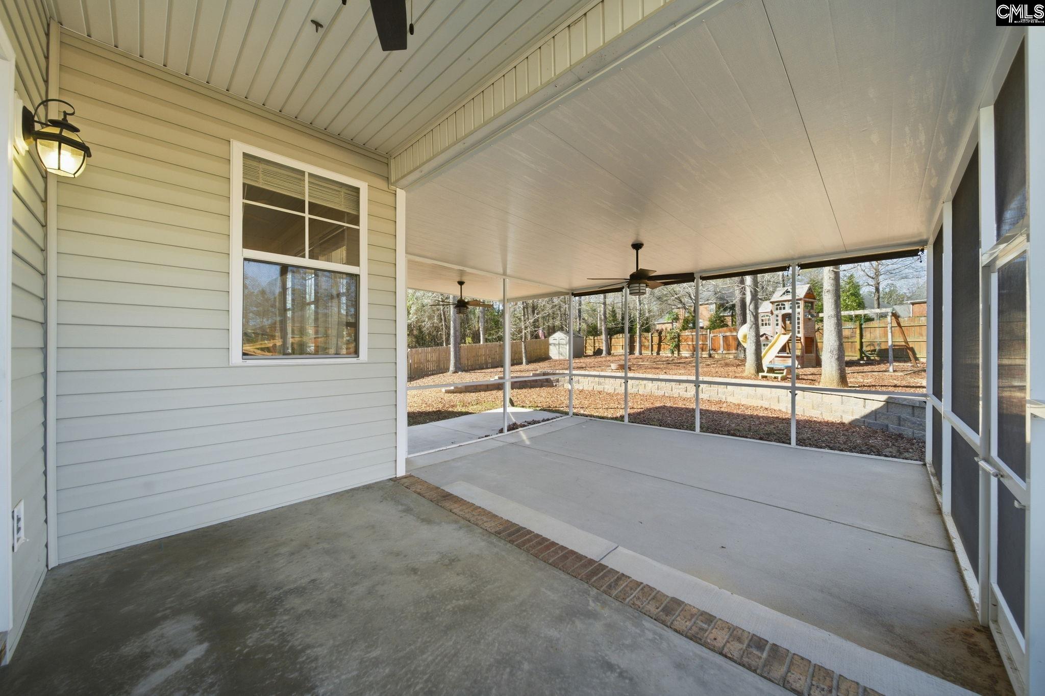 Covered rear patio with ceiling fans and a view of a fenced backyard playset.