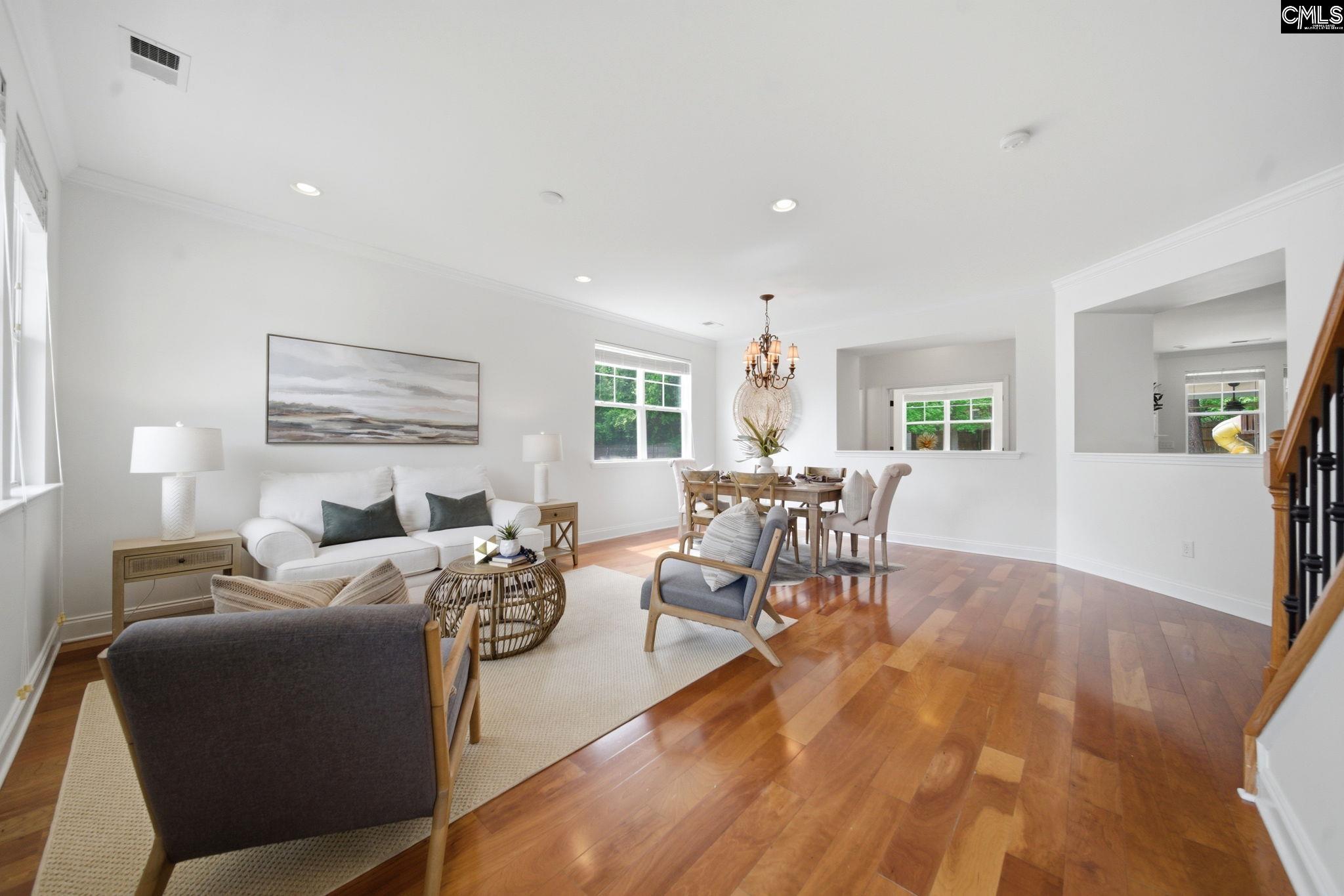 Staged living room with hardwood floors, large windows, and an adjoining dining area.