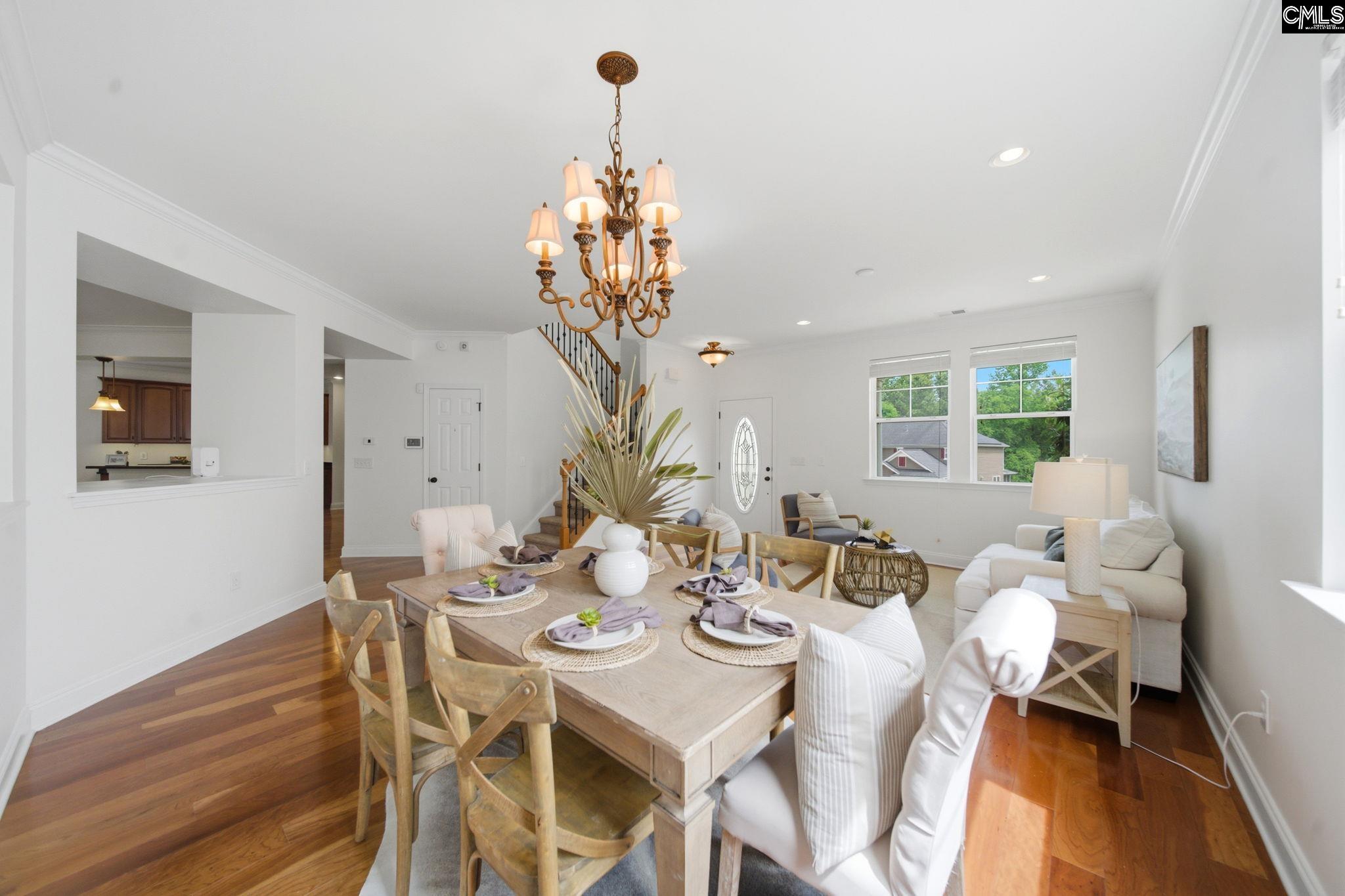 Open-plan living and dining room with a set table, white seating, hardwood floors, and a prominent chandelier.