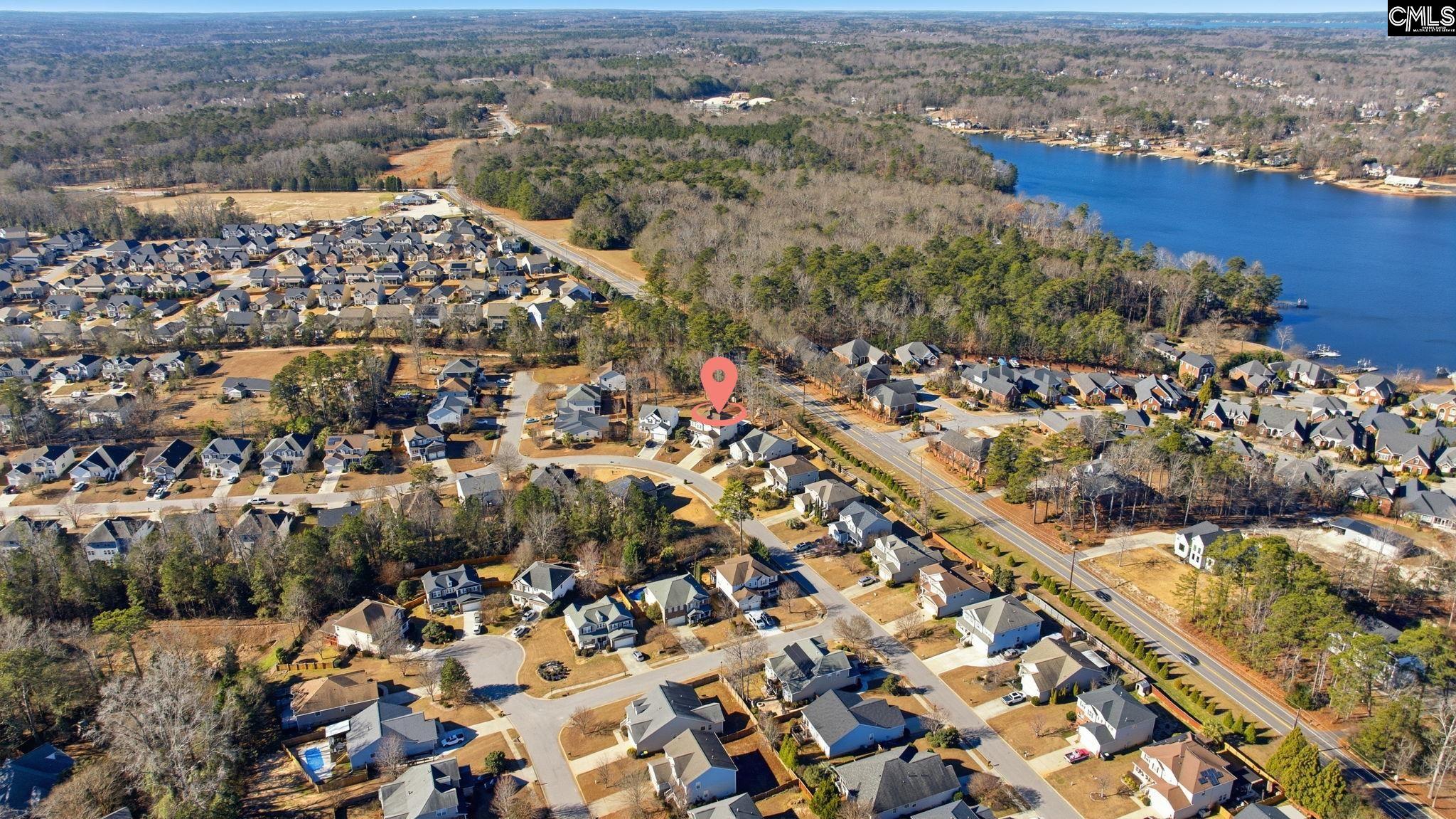 Aerial view of the marked property in a lakeside neighborhood, with wooded shoreline and nearby homes.