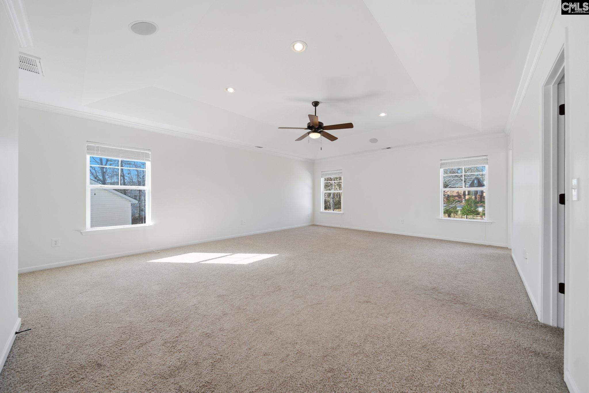 Vacant carpeted room with three windows and a ceiling fan