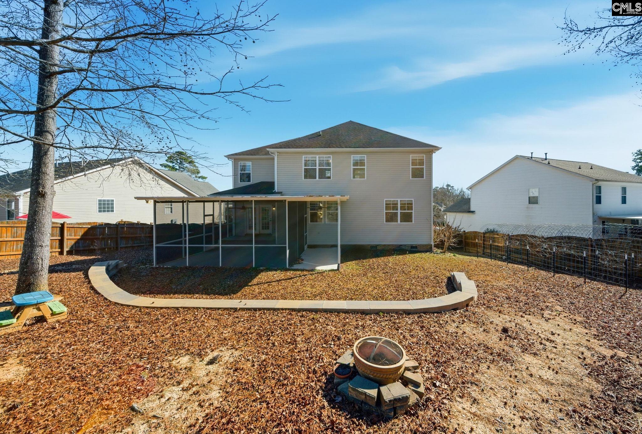 Two-story house viewed from its leaf-covered backyard, with a screened porch and circular fire pit.