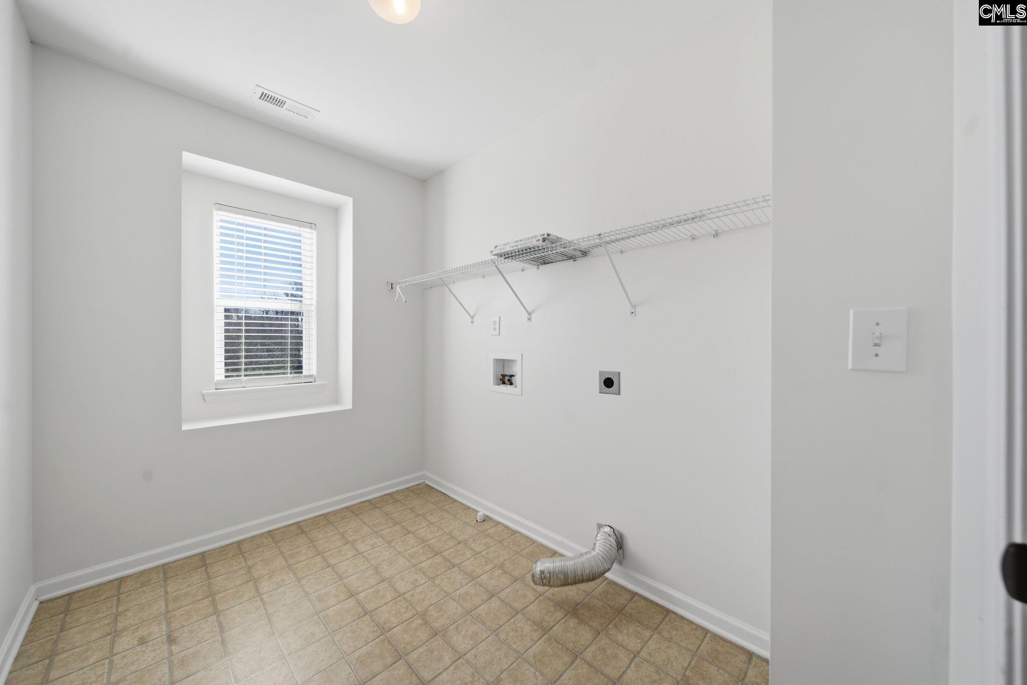 Empty laundry room with tiled floor, wire shelf, washer hookups, and a recessed window.