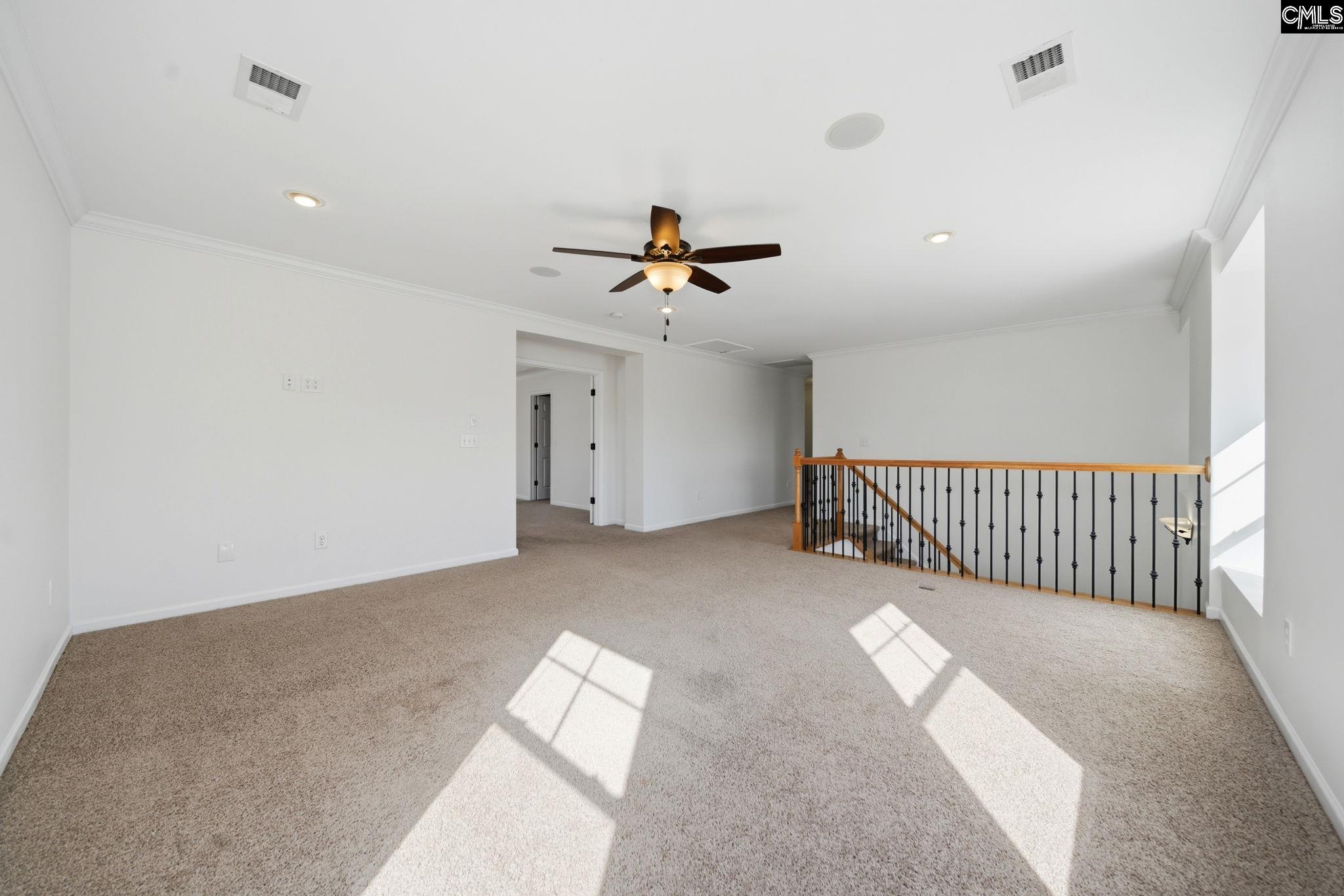 Unfurnished carpeted upstairs loft with a ceiling fan and wood-and-metal stair railing.