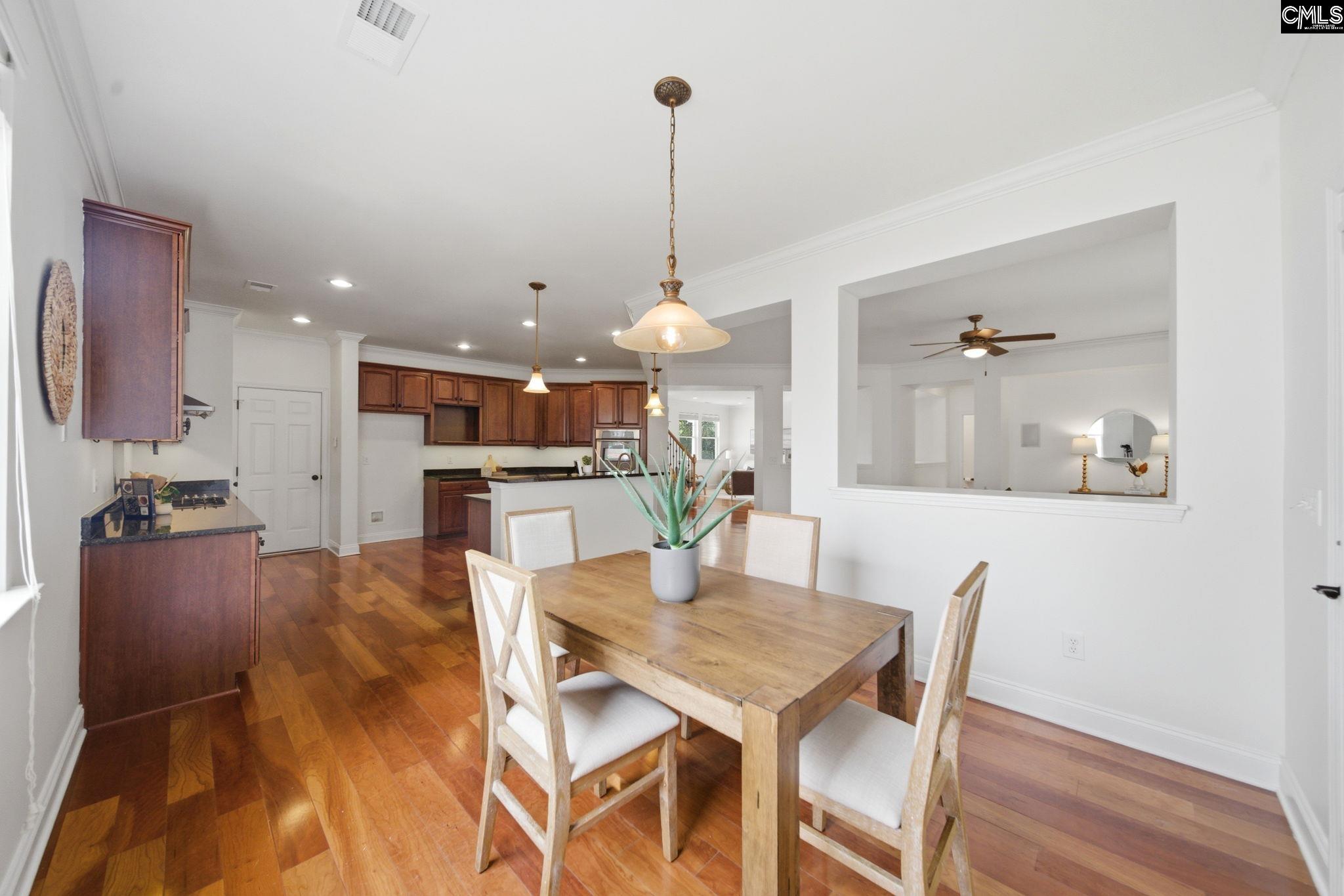 Dining area with a wooden table and hardwood floors, opening to a kitchen with dark wood cabinets.
