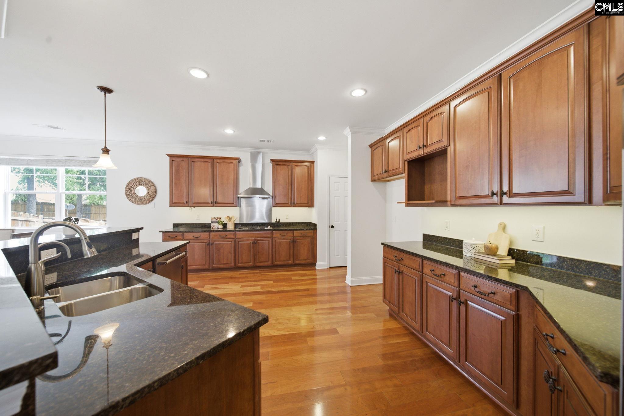 Kitchen with warm wood cabinets, dark granite counters, a central island, and hardwood floors.