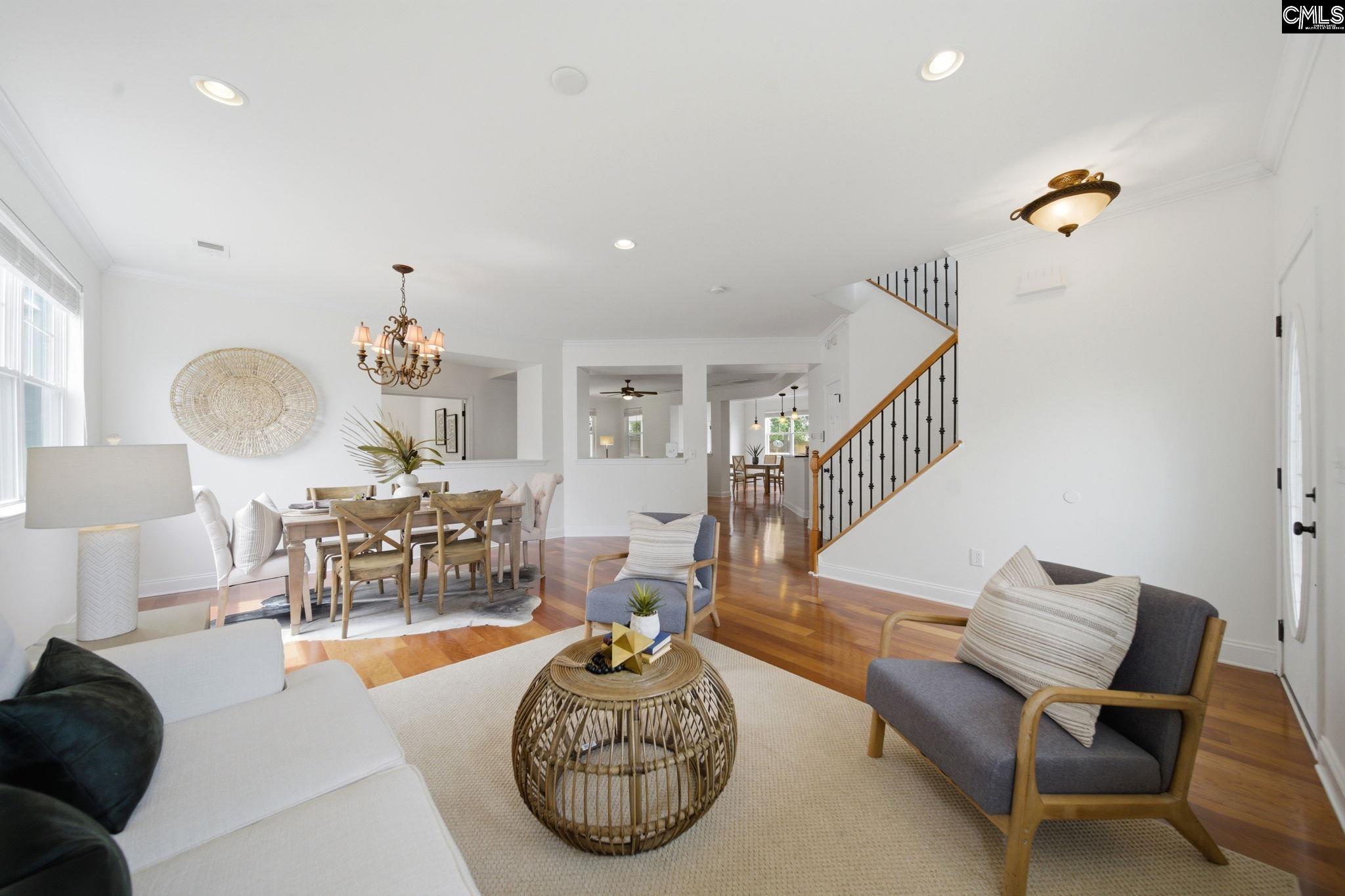 Open living and dining room with hardwood floors, a woven coffee table, and a staircase with black iron balusters.