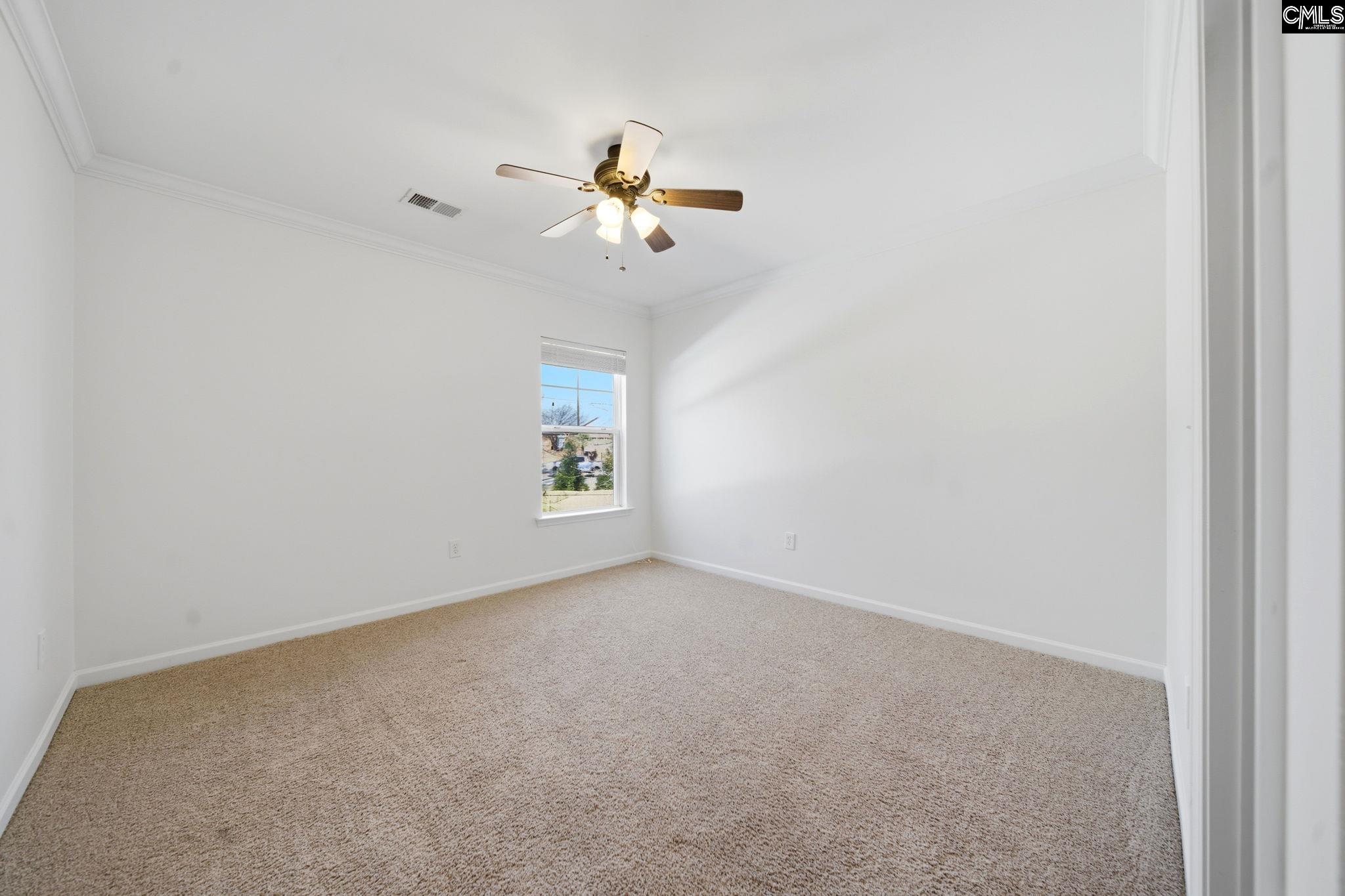 Empty bedroom with beige carpet, a window, and a lit ceiling fan.