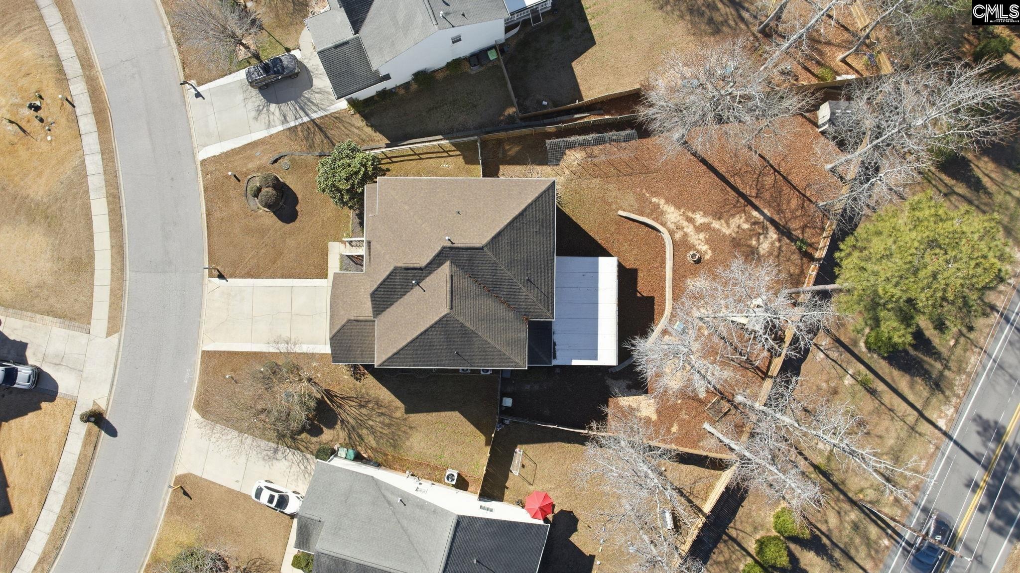 Aerial view of a gray-roofed house with a driveway and fenced, tree-lined backyard.