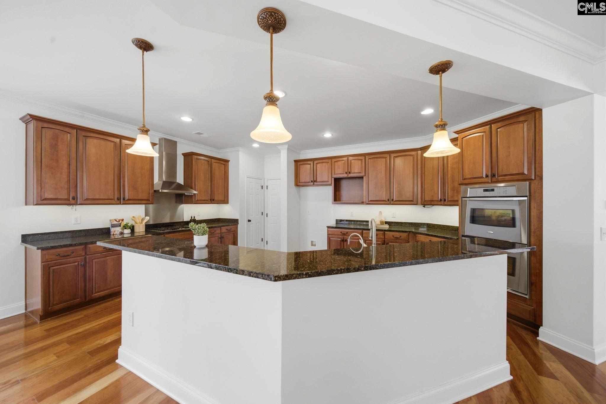 Kitchen with a large granite island, warm wood cabinets, stainless-steel oven, and hardwood floors.