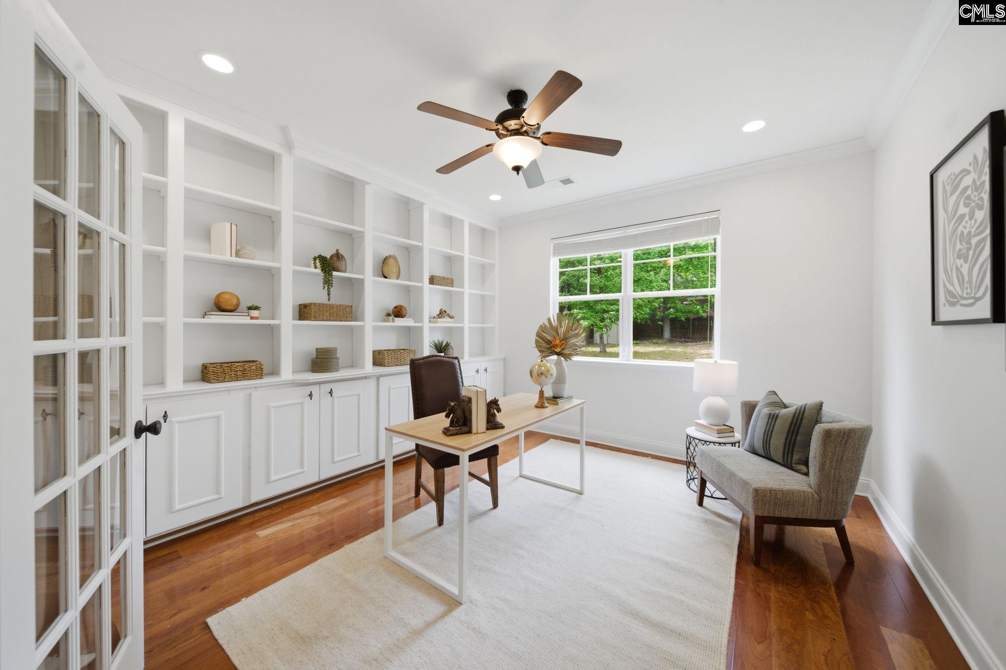 Bright home office with white built-in shelves, a desk, and an armchair beside a window.