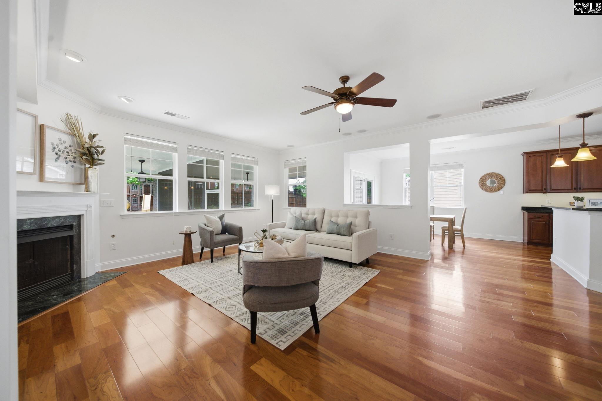 Staged living room with a white fireplace, large windows, and warm hardwood floors.