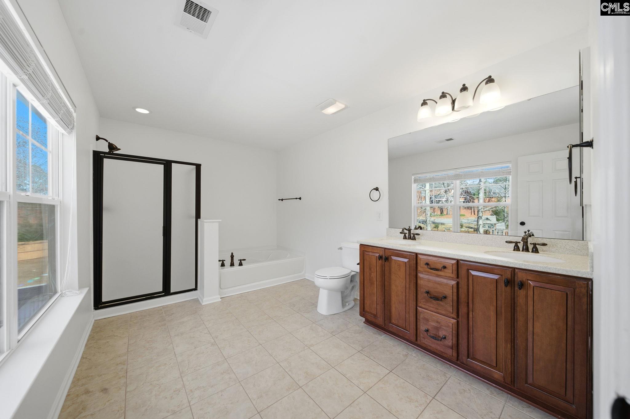 Bathroom with double-sink wood vanity, large mirror, bathtub, and black-framed glass shower.