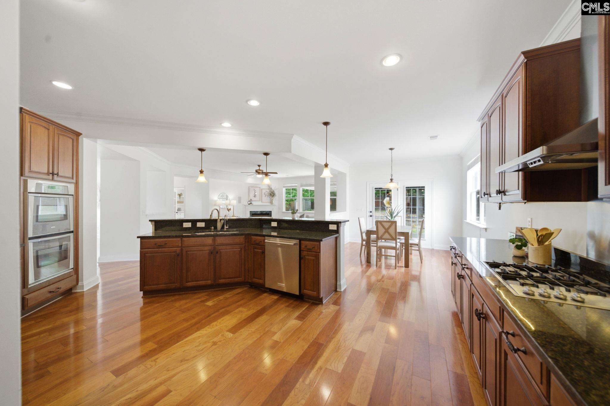 Open kitchen with dark wood cabinets, granite island, stainless appliances, and hardwood floors.