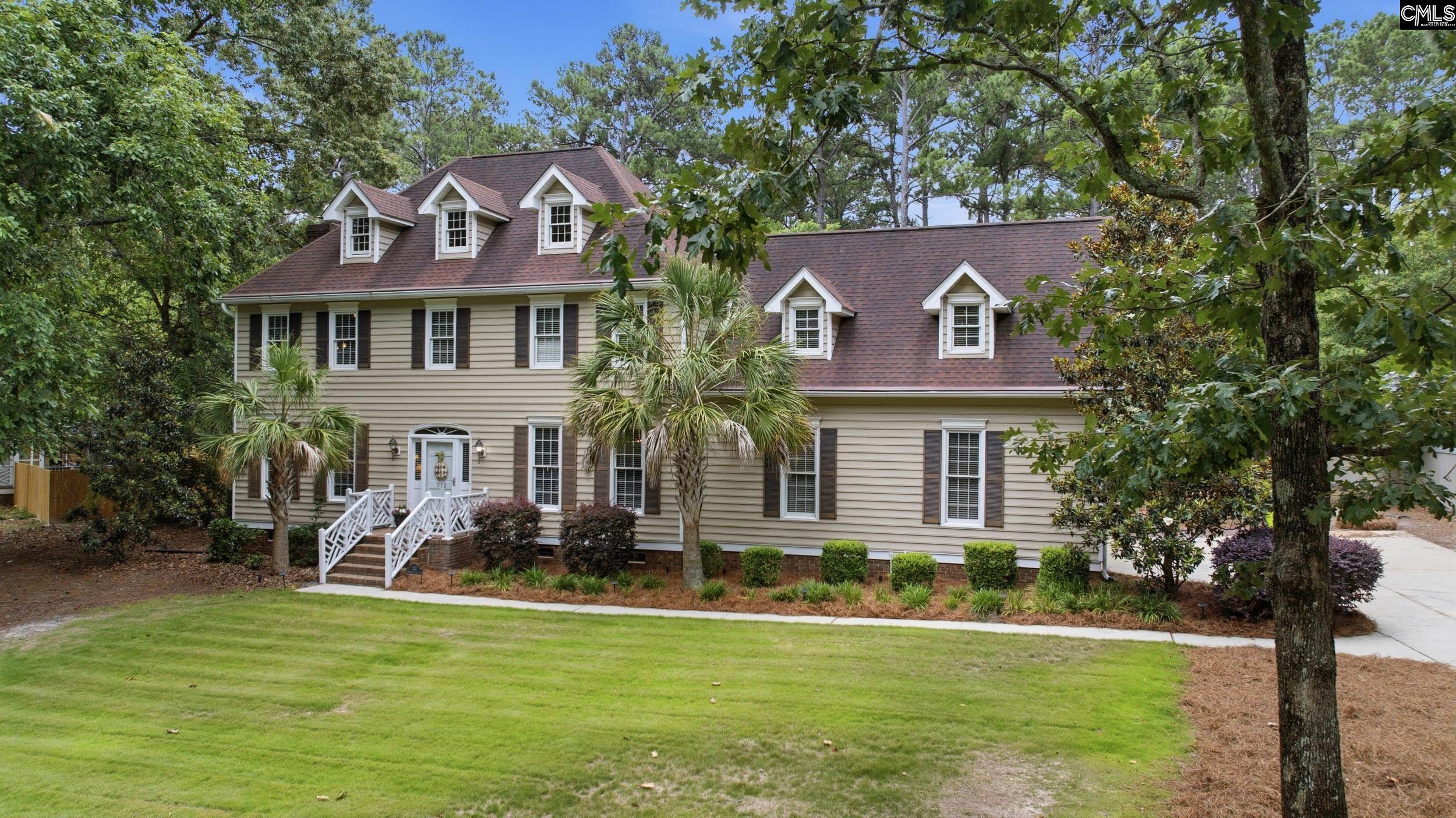 Two-story beige home with dormer windows, a white entry stairway, and mature trees.