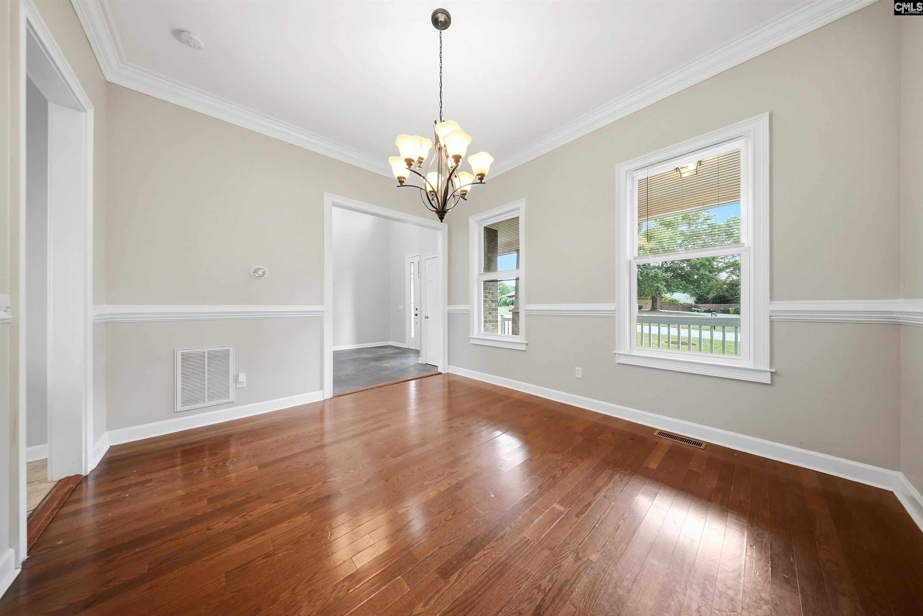 Empty dining room with hardwood floors, a chandelier, and windows overlooking the front porch.