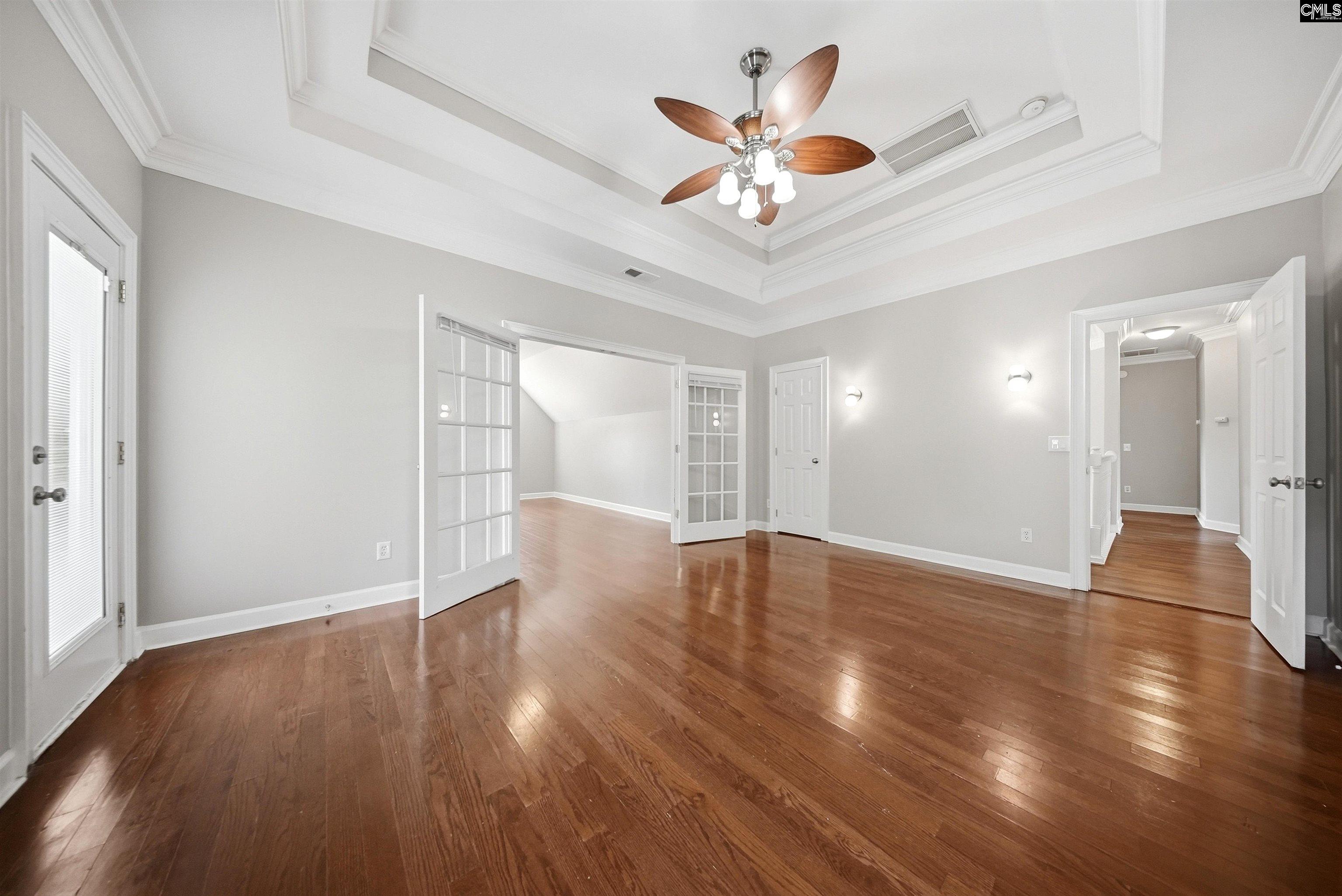 Empty room with hardwood floors, a tray ceiling, and open French doors.