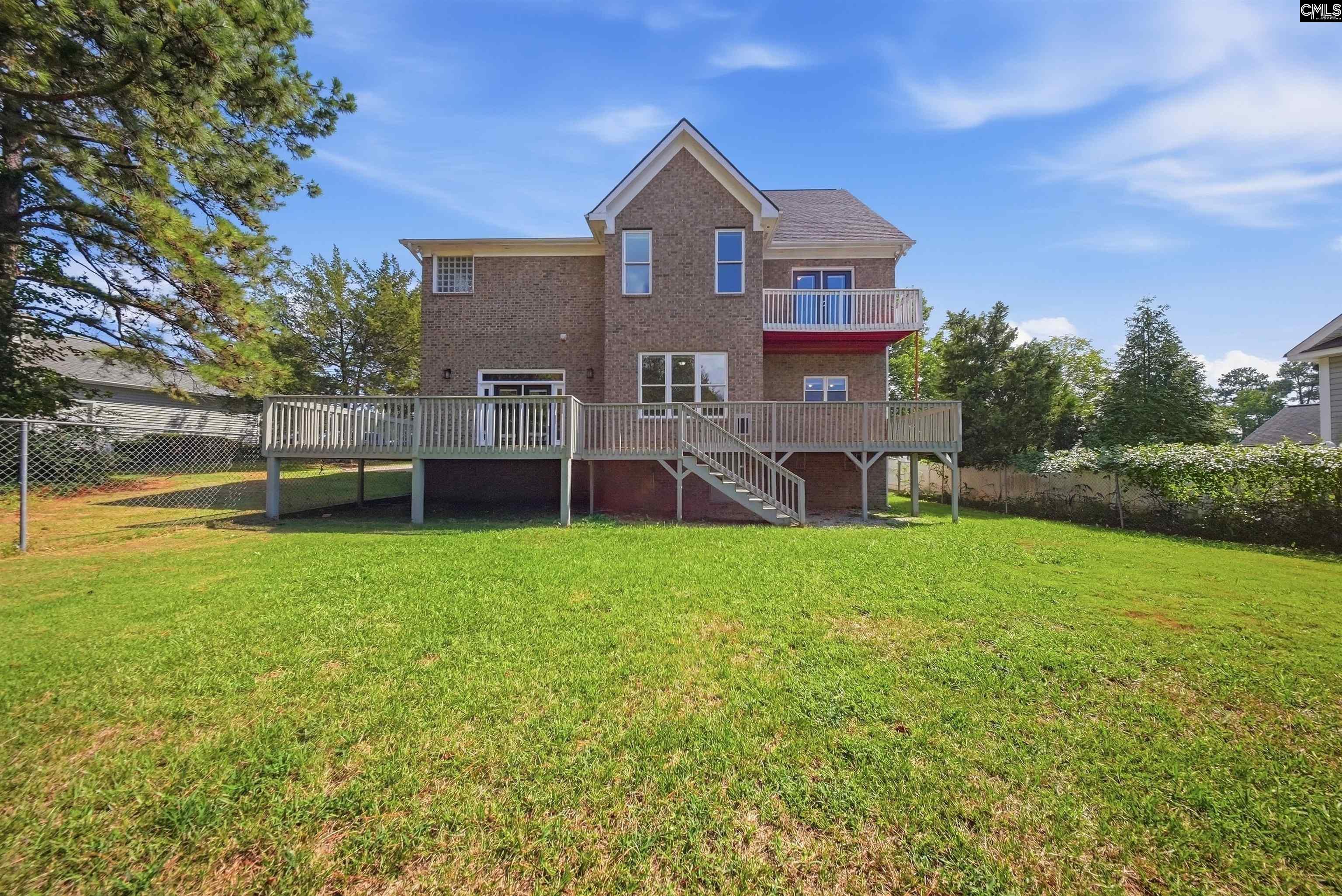 Two-story brick home with a wide raised deck and stairs overlooking a green backyard.