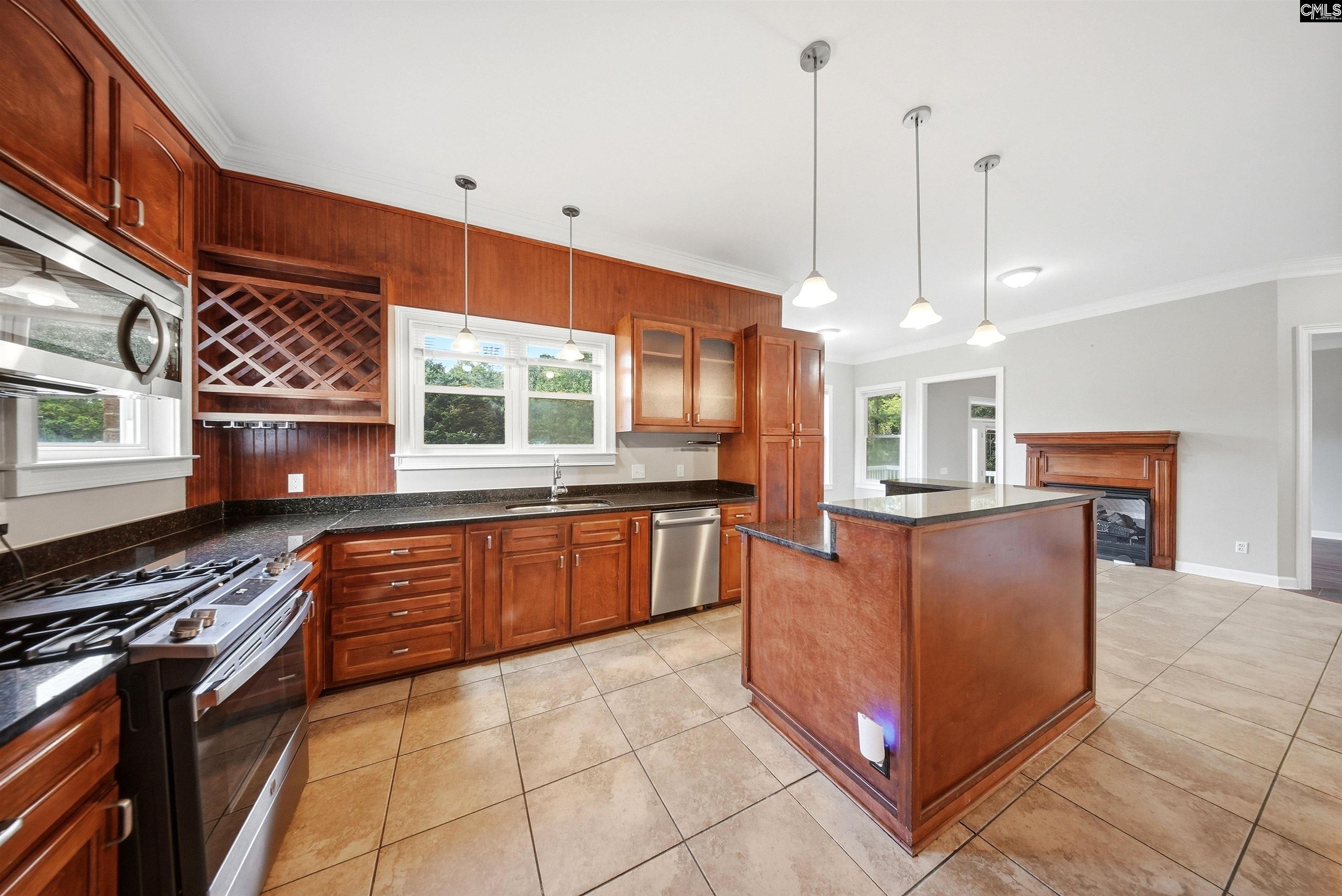 Kitchen with warm wood cabinetry, black countertops, stainless steel appliances, and a central island.