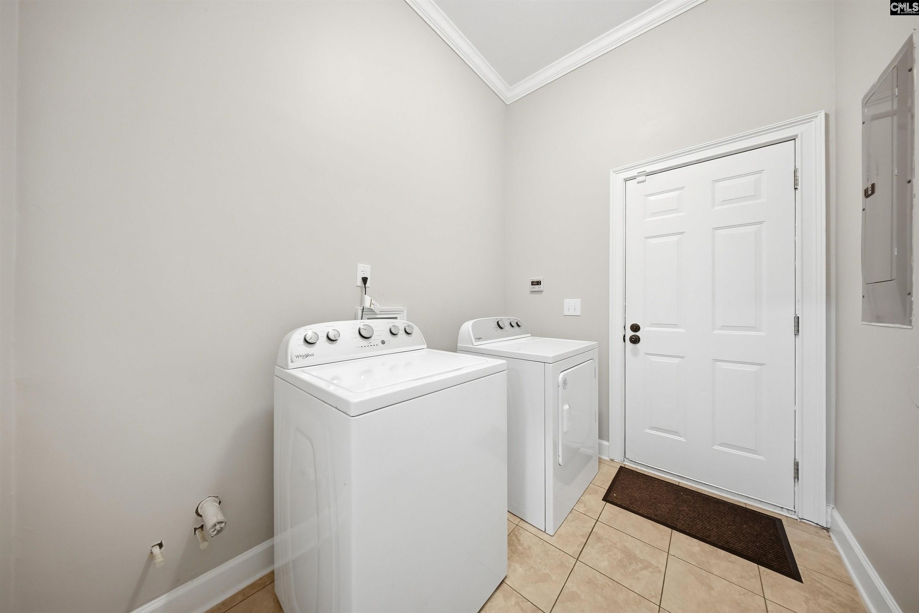 Laundry room with a white washer and dryer, beige tile floor, and white paneled door.