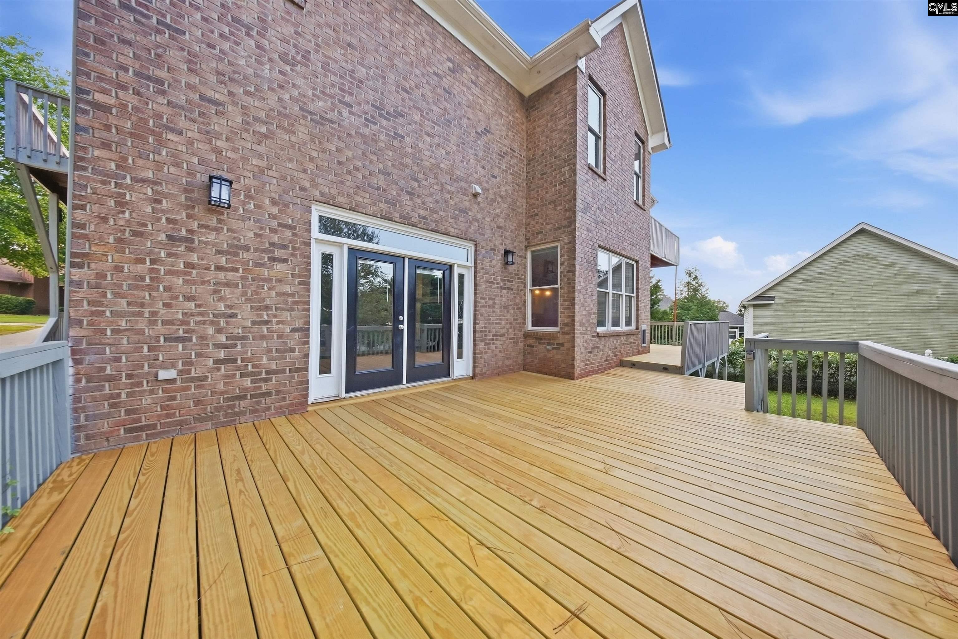 Spacious wooden rear deck along a two-story brick house, with patio doors and gray railings.
