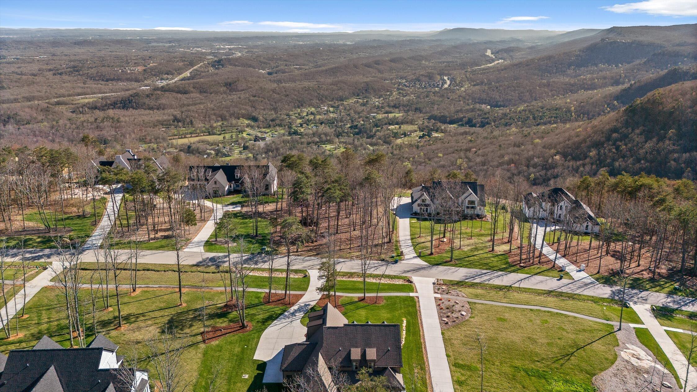 Aerial view of homes along winding streets, with wooded hills and a broad mountain valley beyond.